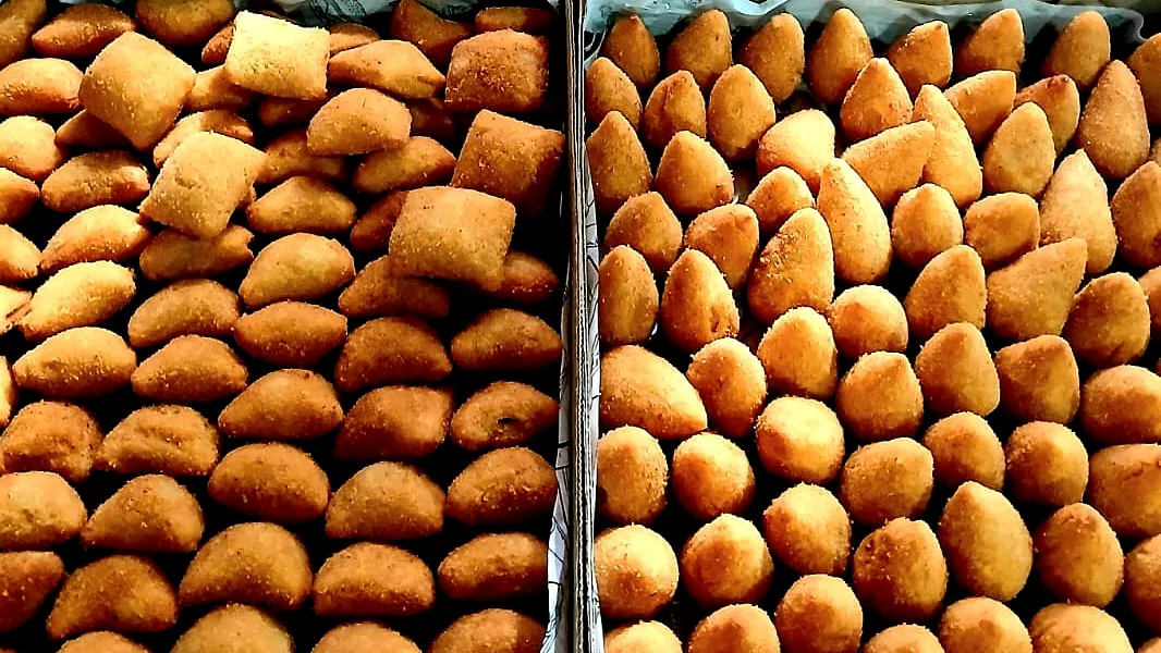 Duas bandejas cheias de coxinhas douradas e croquetes, recém-fritos e alinhados na caixa